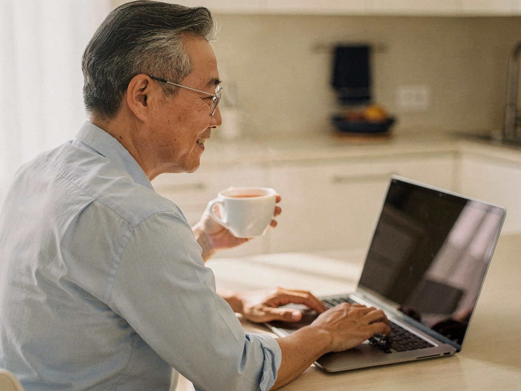 A man at his kitchen table with a cup of tea, working calmly on a laptop