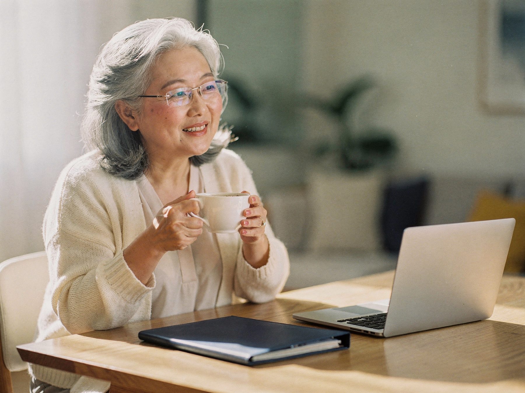 A woman holding a cup of tea at a sunlit table, relaxed